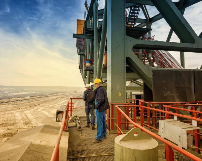 Two men standing on intermediate platform on large mining shovel.