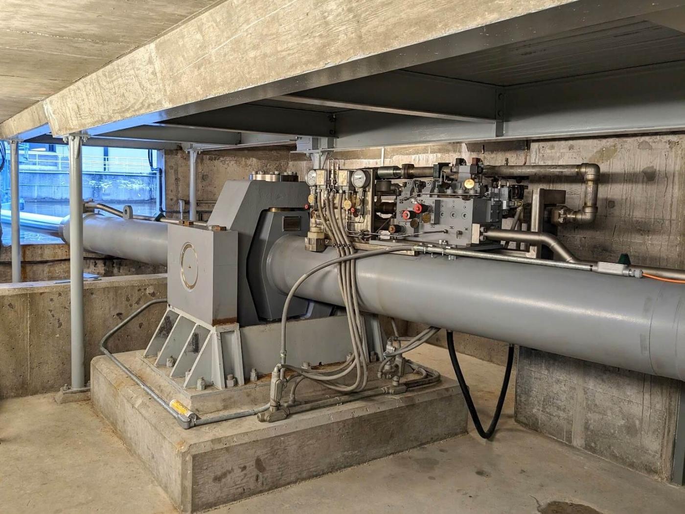 Custom large bore cylinder with gimbal and onboard valve assembly for a lock miter gate installed in a machinery room.