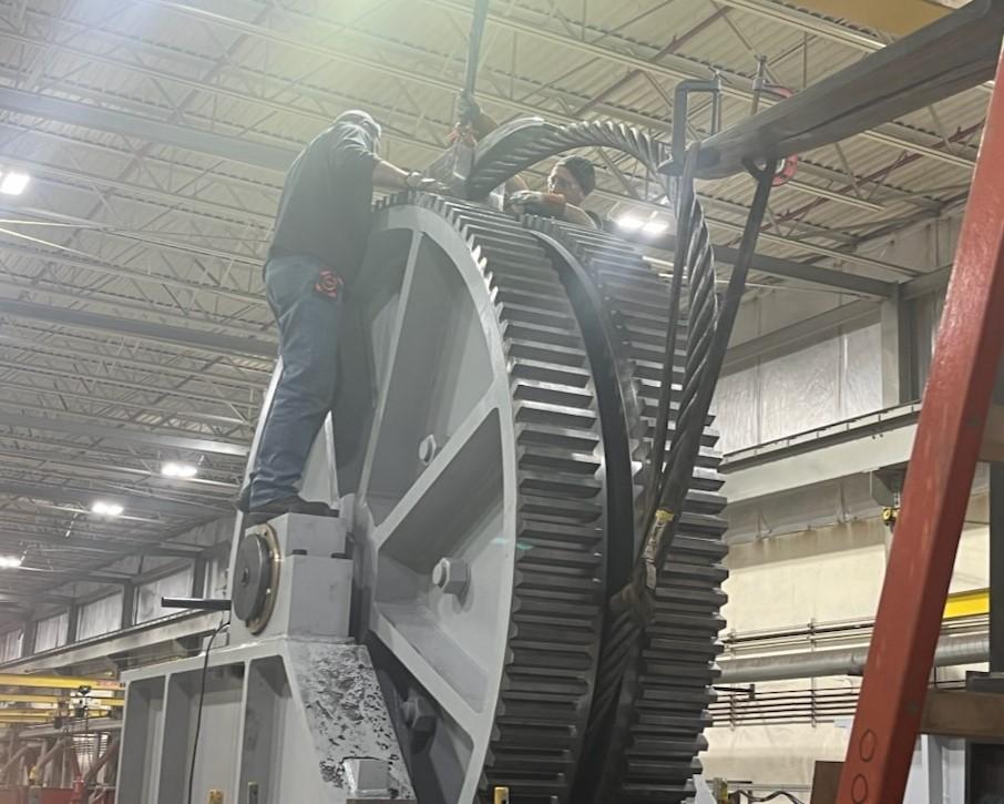 Two millwrights preparing ship arrestor for load test with heavy duty hydraulic cylinder in shop.