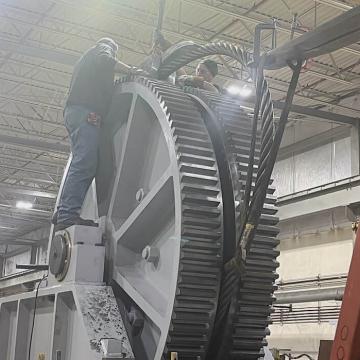 Two millwrights assembling large diameter bull gear and wire rope on ship arrestor frame in shop